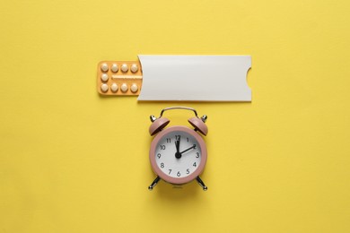 Oral contraceptive pills and alarm clock on yellow background, flat lay