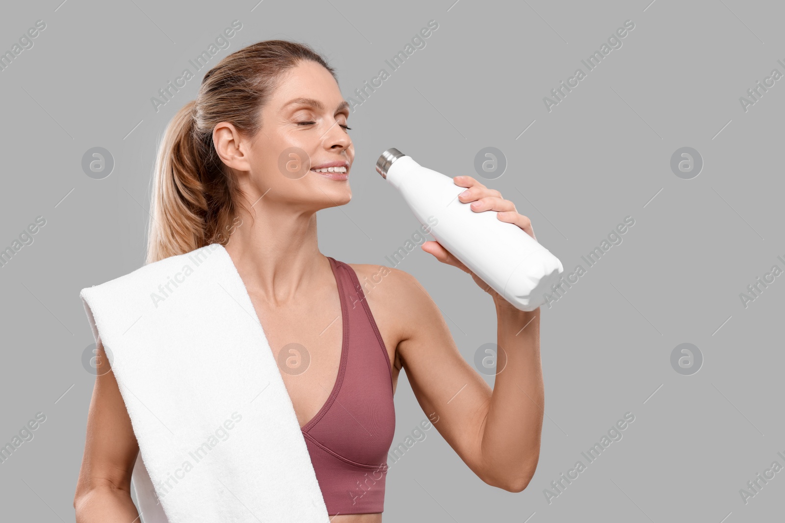 Photo of Sportswoman with thermo bottle and white towel on grey background, space for text