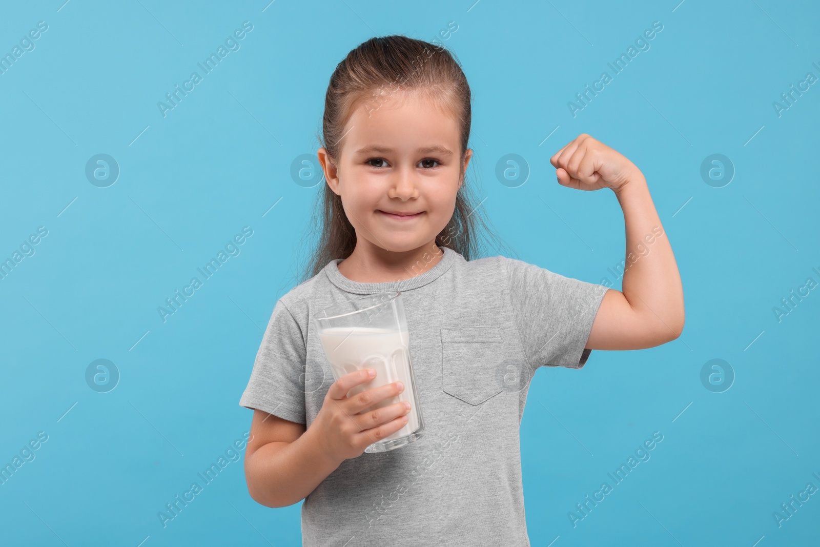 Photo of Cute girl with glass of fresh milk showing her strength on light blue background