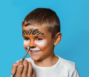 Artist painting face of little boy on blue background