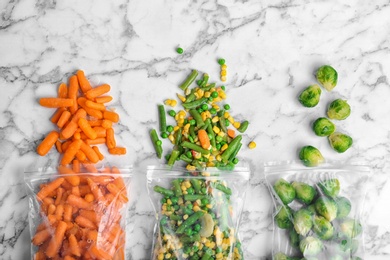 Photo of Plastic bags with different frozen vegetables on marble table, top view
