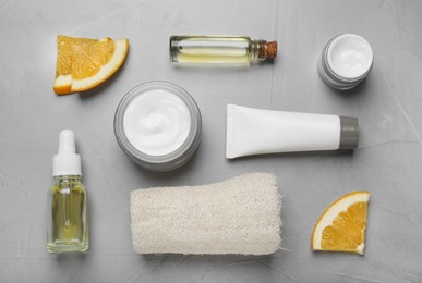 Photo of Body cream and other cosmetic products with orange on light grey table, flat lay
