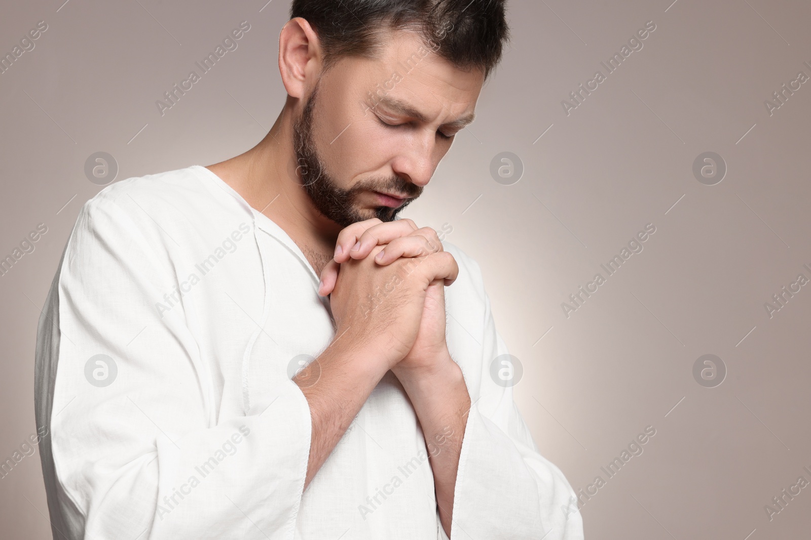 Photo of Religious man with clasped hands praying against grey background. Space for text