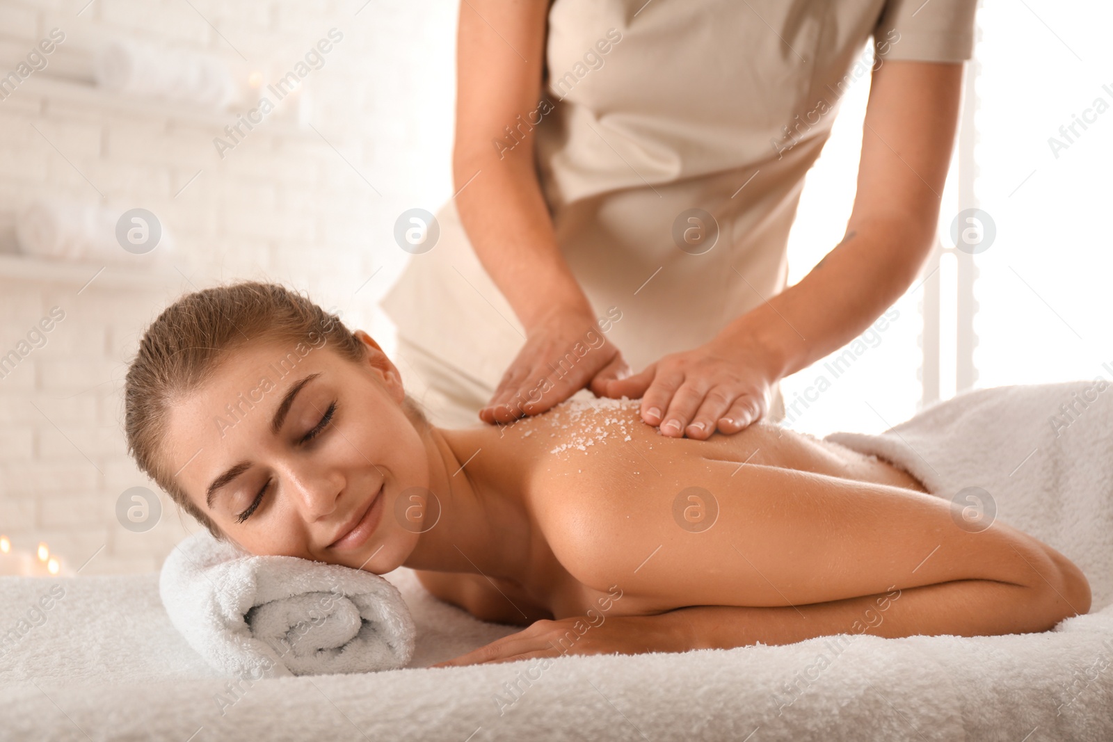 Photo of Young woman having body scrubbing procedure with sea salt in spa salon