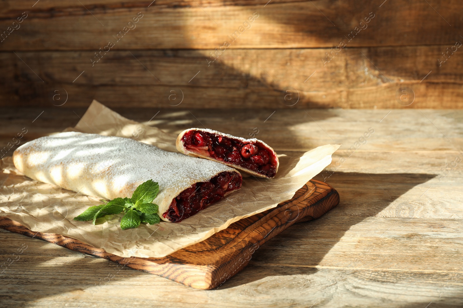 Photo of Delicious strudel with cherries, powdered sugar and mint on wooden table. Space for text