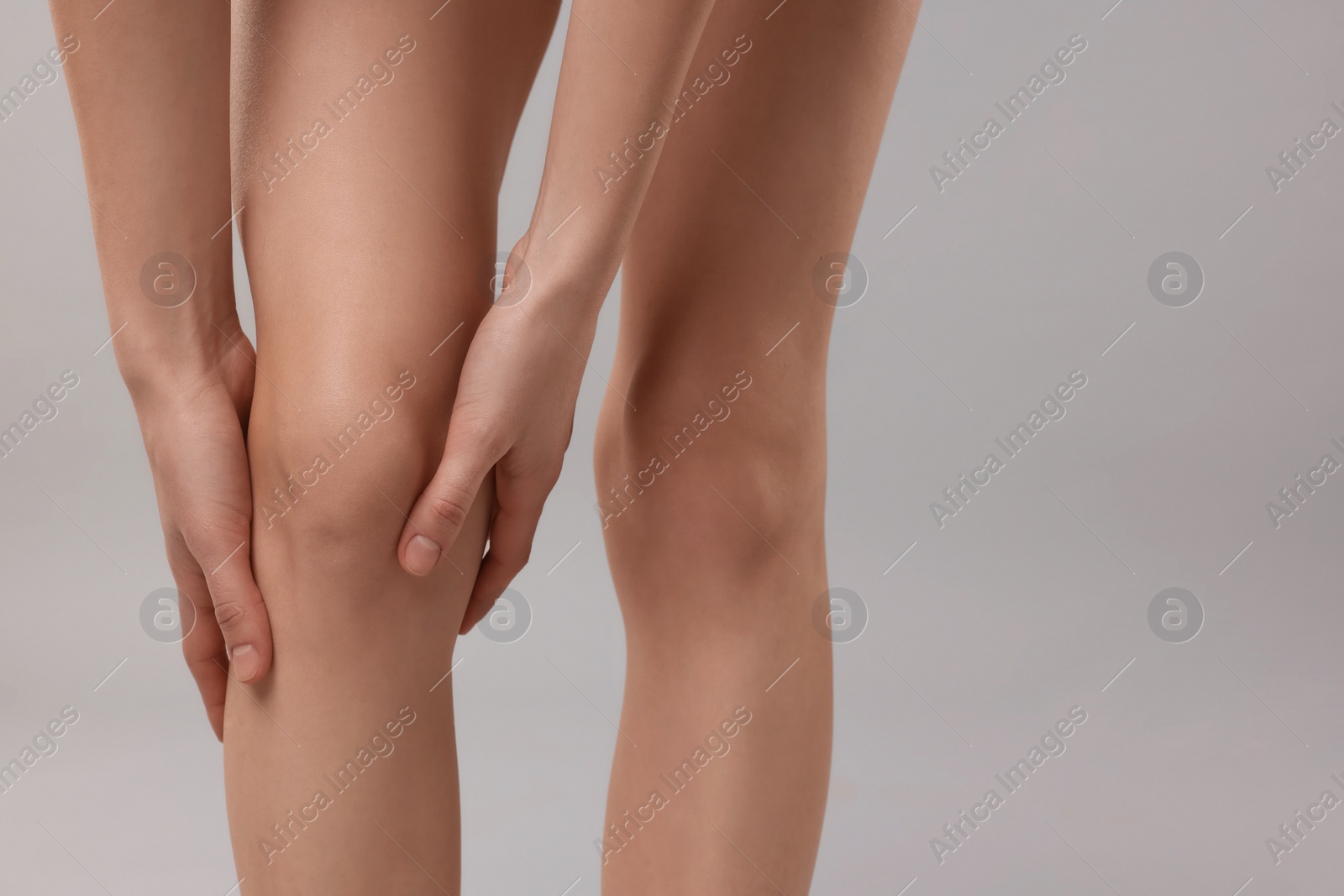 Photo of Woman suffering from leg pain on grey background, closeup. Space for text