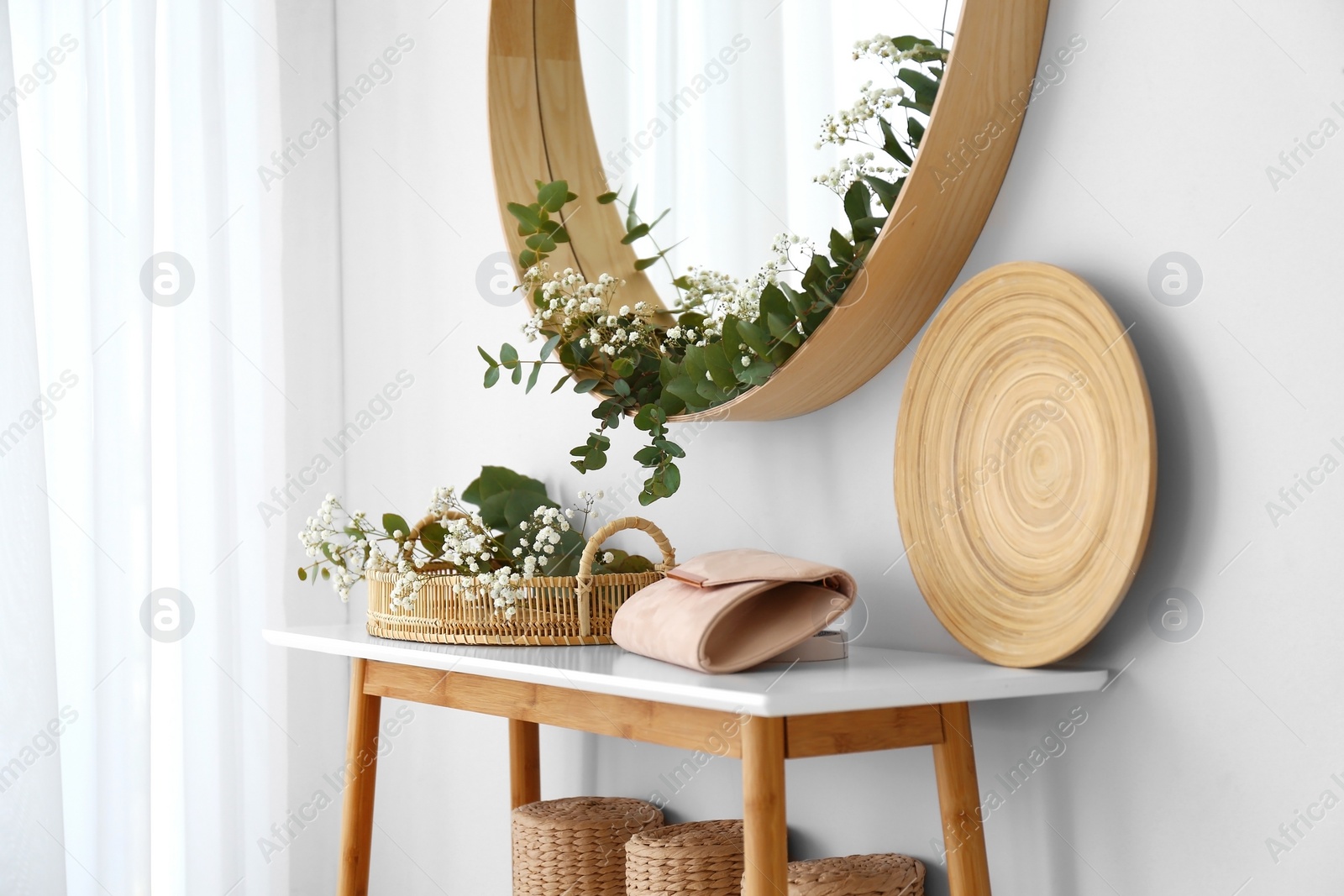 Photo of Round mirror and table with accessories near white wall. Modern interior design