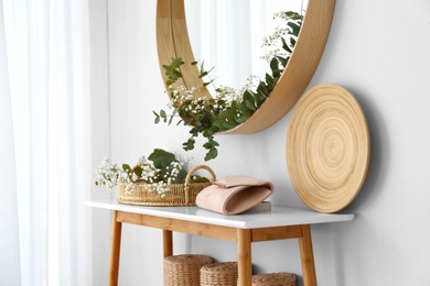 Round mirror and table with accessories near white wall. Modern interior design