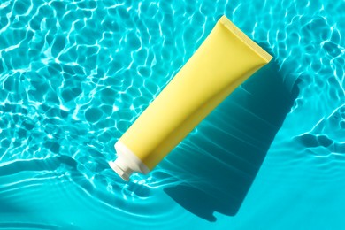 Photo of Tube with moisturizing cream in water on light blue background, top view