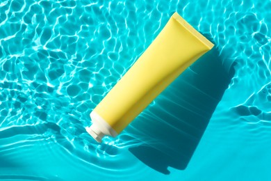 Tube with moisturizing cream in water on light blue background, top view