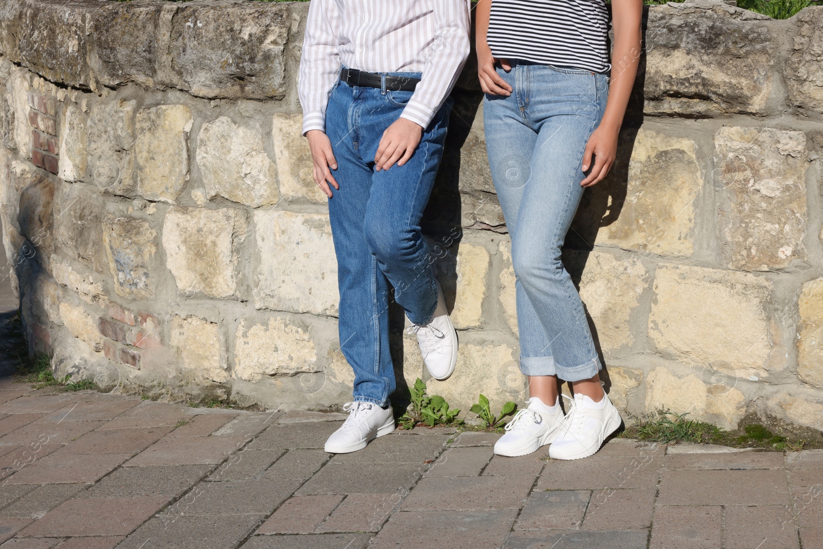 Photo of People in stylish jeans near stone wall outdoors on sunny day, closeup