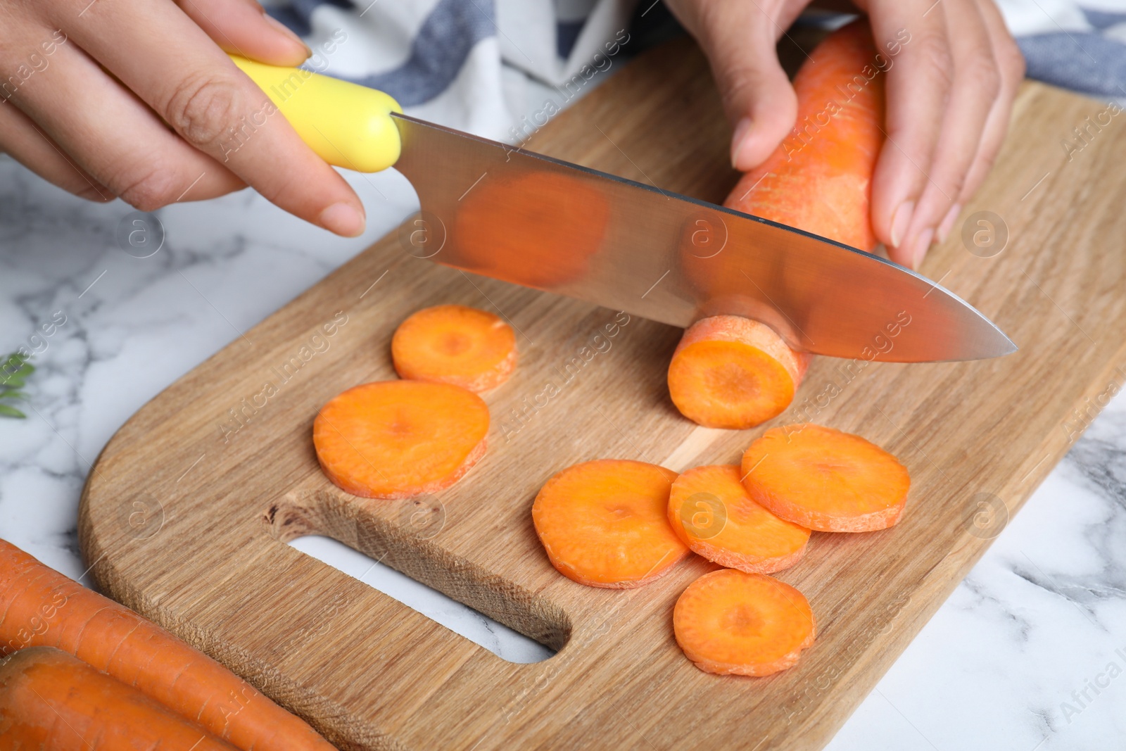 Photo of Woman cutting ripe carrot on wooden board at white marble table, closeup