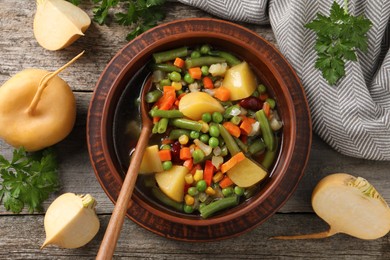 Photo of Bowl of delicious turnip soup served on wooden table, flat lay