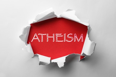 Word Atheism on red background, view through hole in white paper