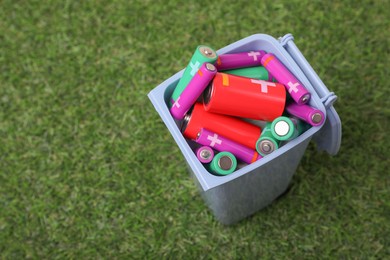 Photo of Many used batteries in recycling bin on green grass, above view. Space for text