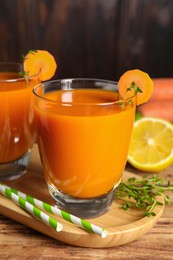 Photo of Glasses of tasty carrot juice and ingredients on wooden table, closeup