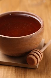 Delicious honey in bowl and dipper on wooden table, closeup