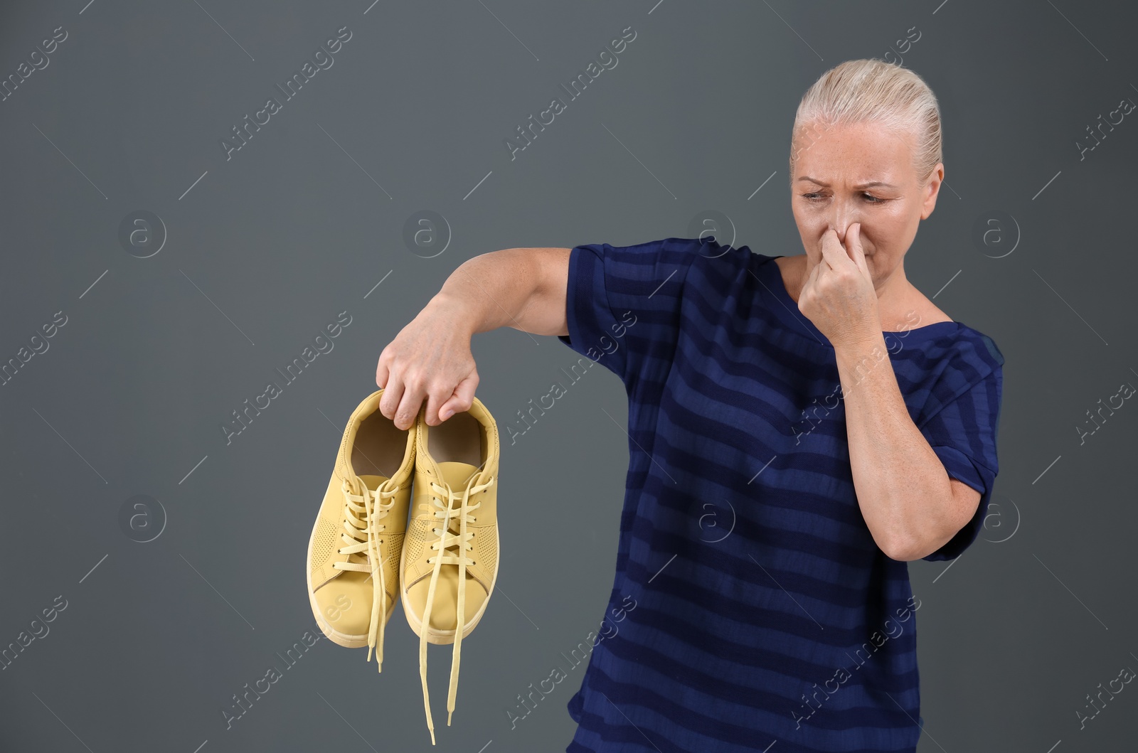 Photo of Woman feeling bad smell from shoes on color background. Air freshener