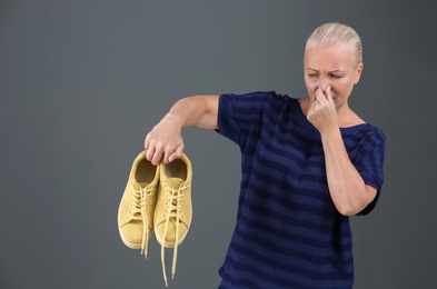 Woman feeling bad smell from shoes on color background. Air freshener