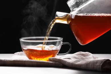 Pouring tea into glass cup on table against black background