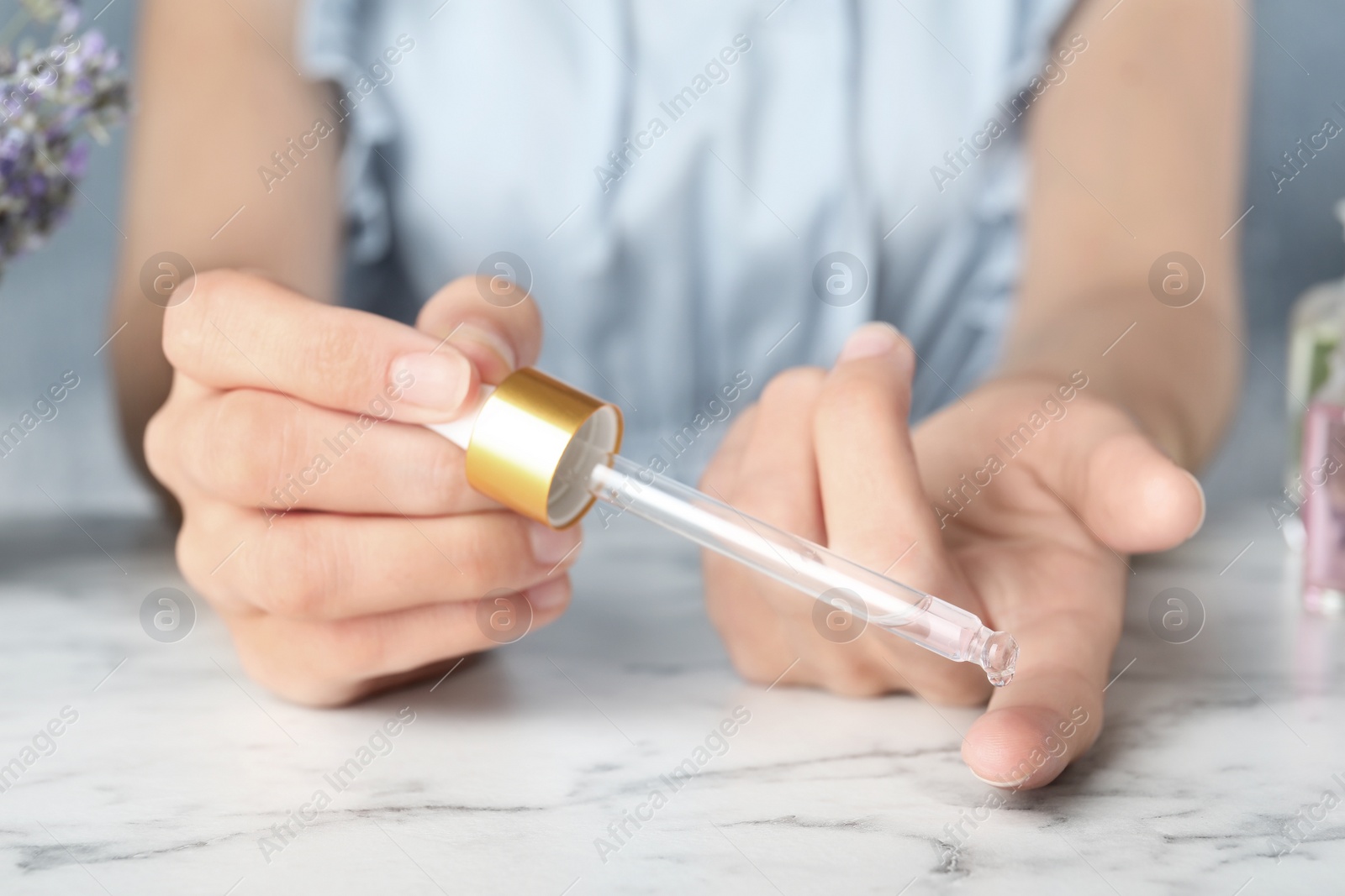 Photo of Woman holding dropper with lavender essential oil at marble table, closeup