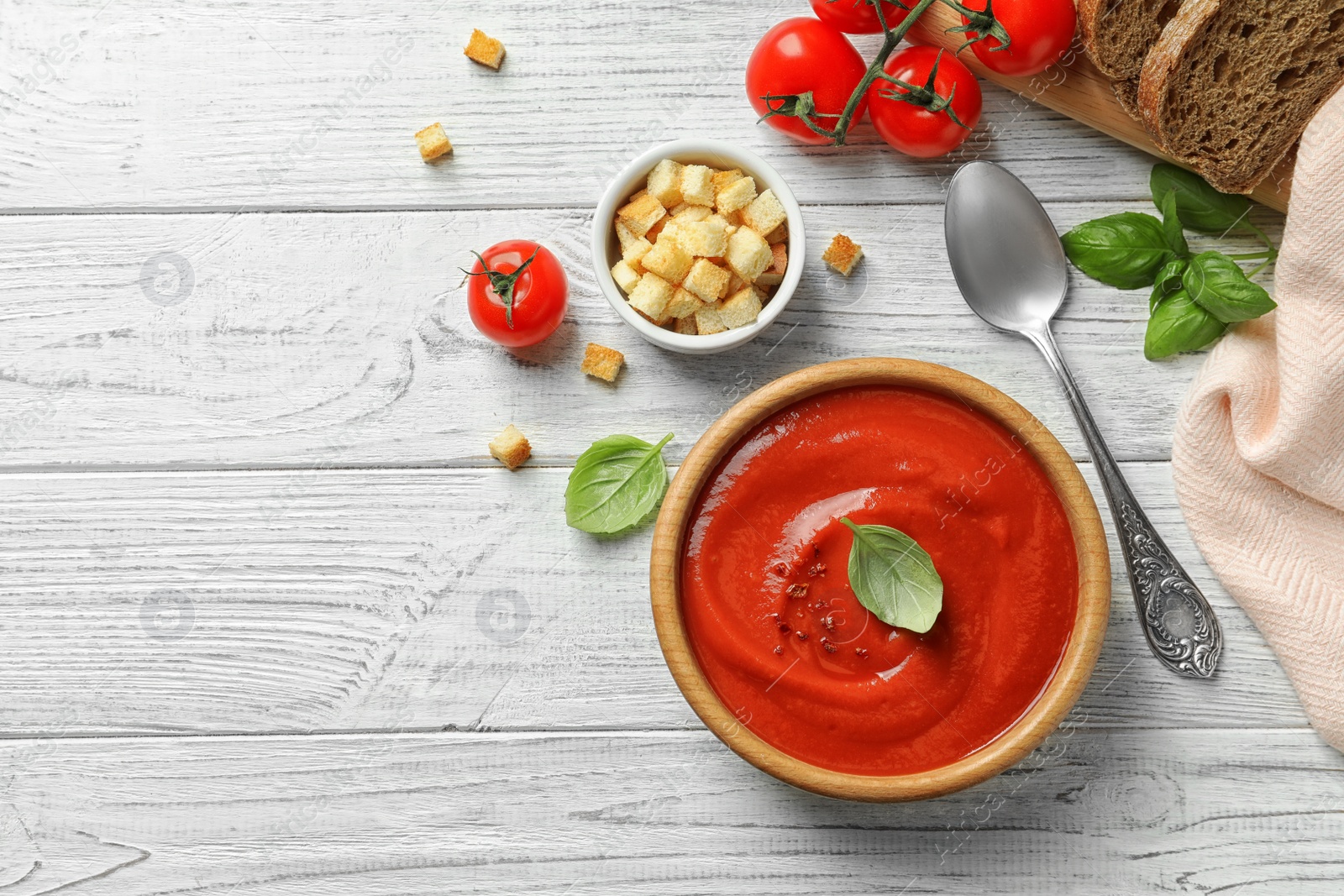 Photo of Fresh homemade tomato soup served with bread and croutons on white wooden table, top view. Space for text