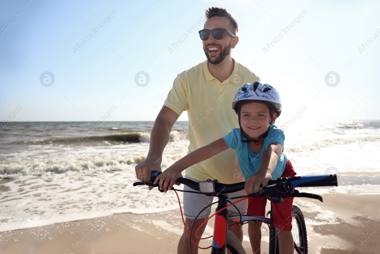 Photo of Happy father teaching son to ride bicycle on sandy beach near sea