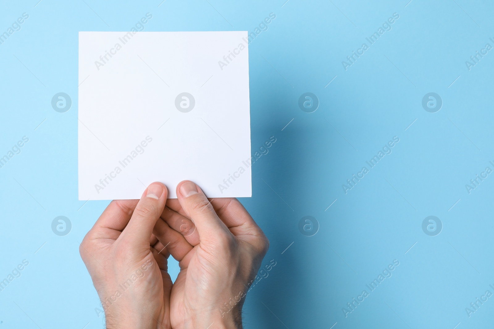 Photo of Man holding sheet of paper on light blue background, top view. Mockup for design