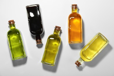 Photo of Vegetable fats. Different cooking oils in glass bottles on white background, flat lay