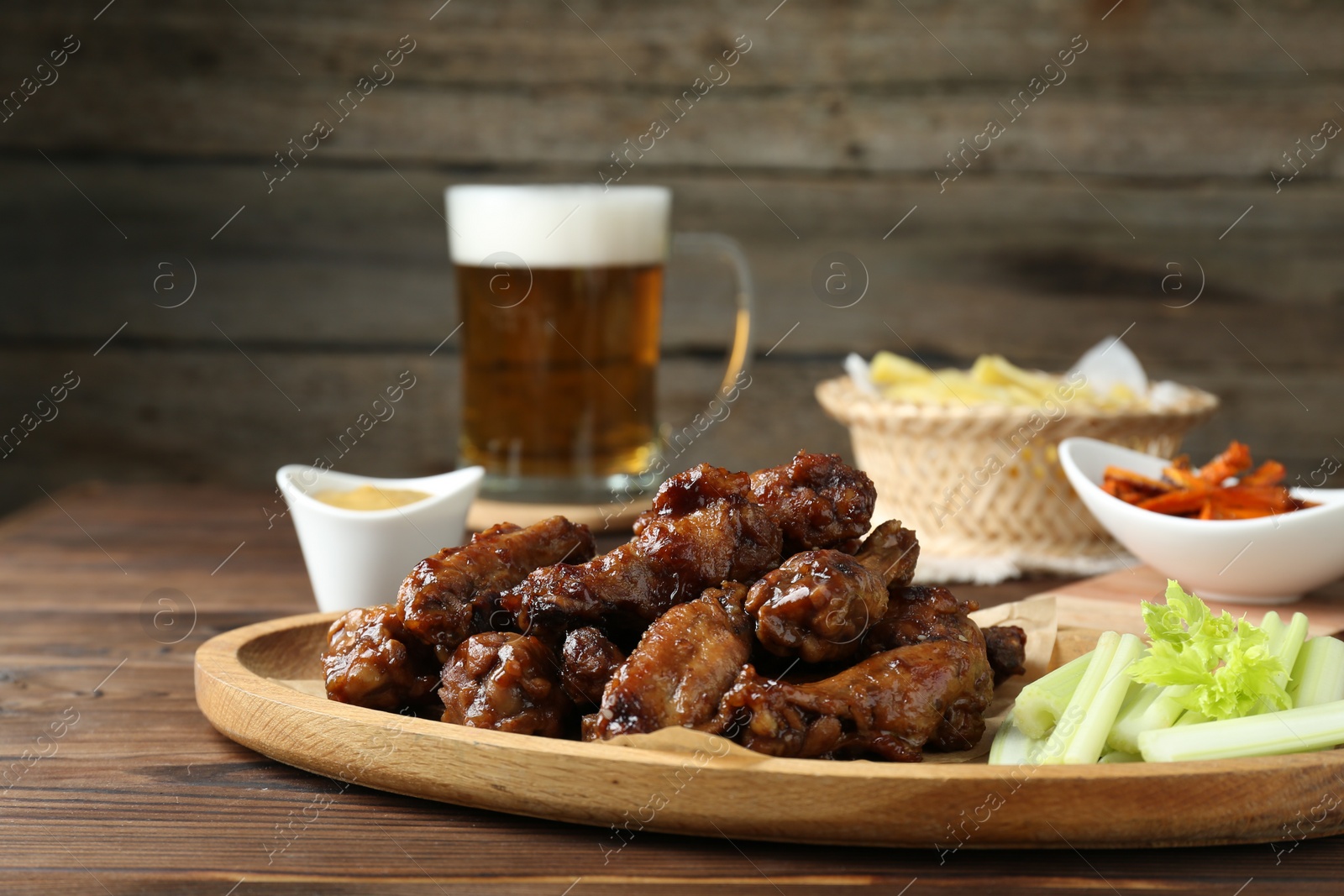 Photo of Delicious chicken wings served with beer on wooden table, closeup