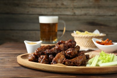 Delicious chicken wings served with beer on wooden table, closeup