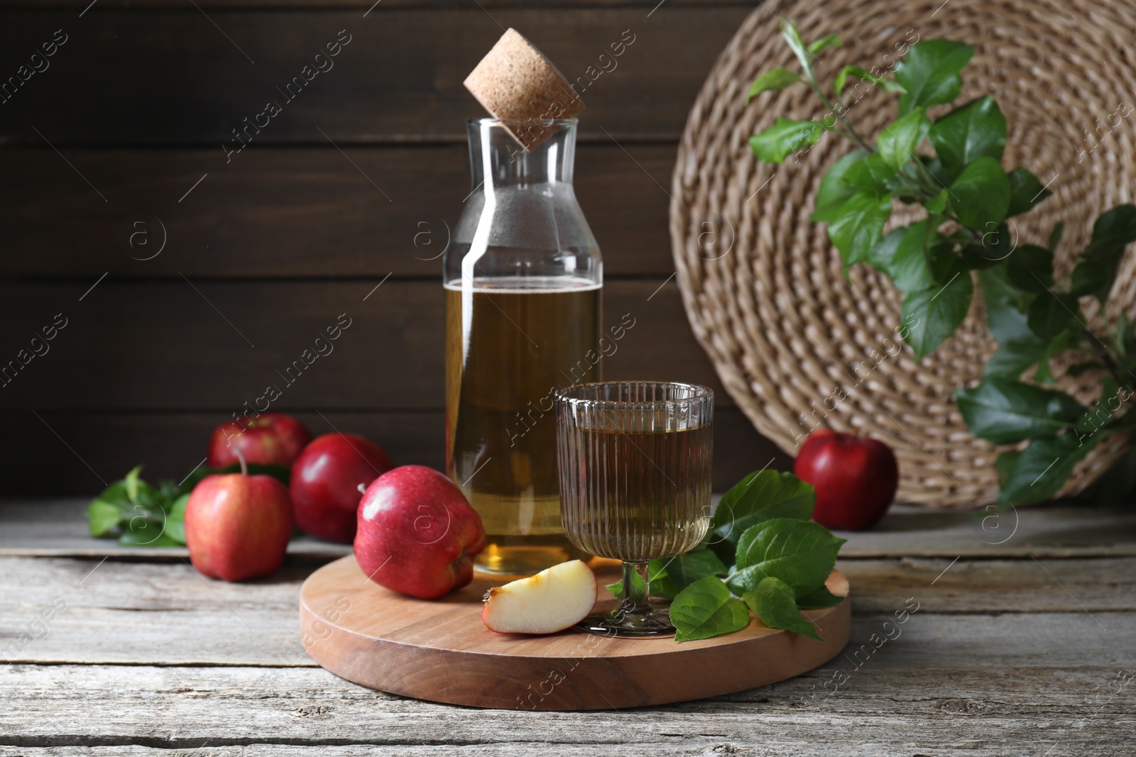 Photo of Delicious cider and apples with green leaves on wooden table