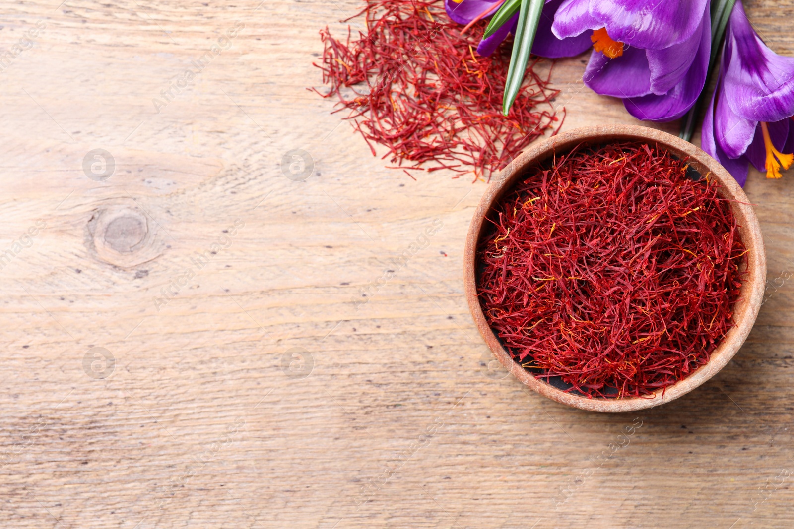 Photo of Dried saffron and crocus flowers on wooden table, flat lay. Space for text