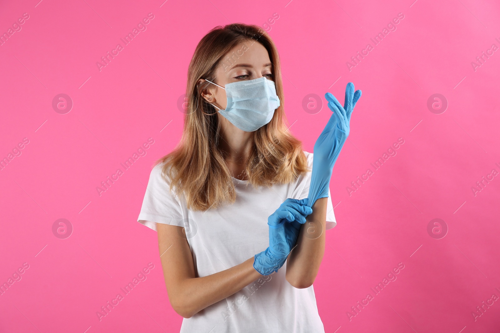 Photo of Young woman in protective mask putting on medical gloves against pink background