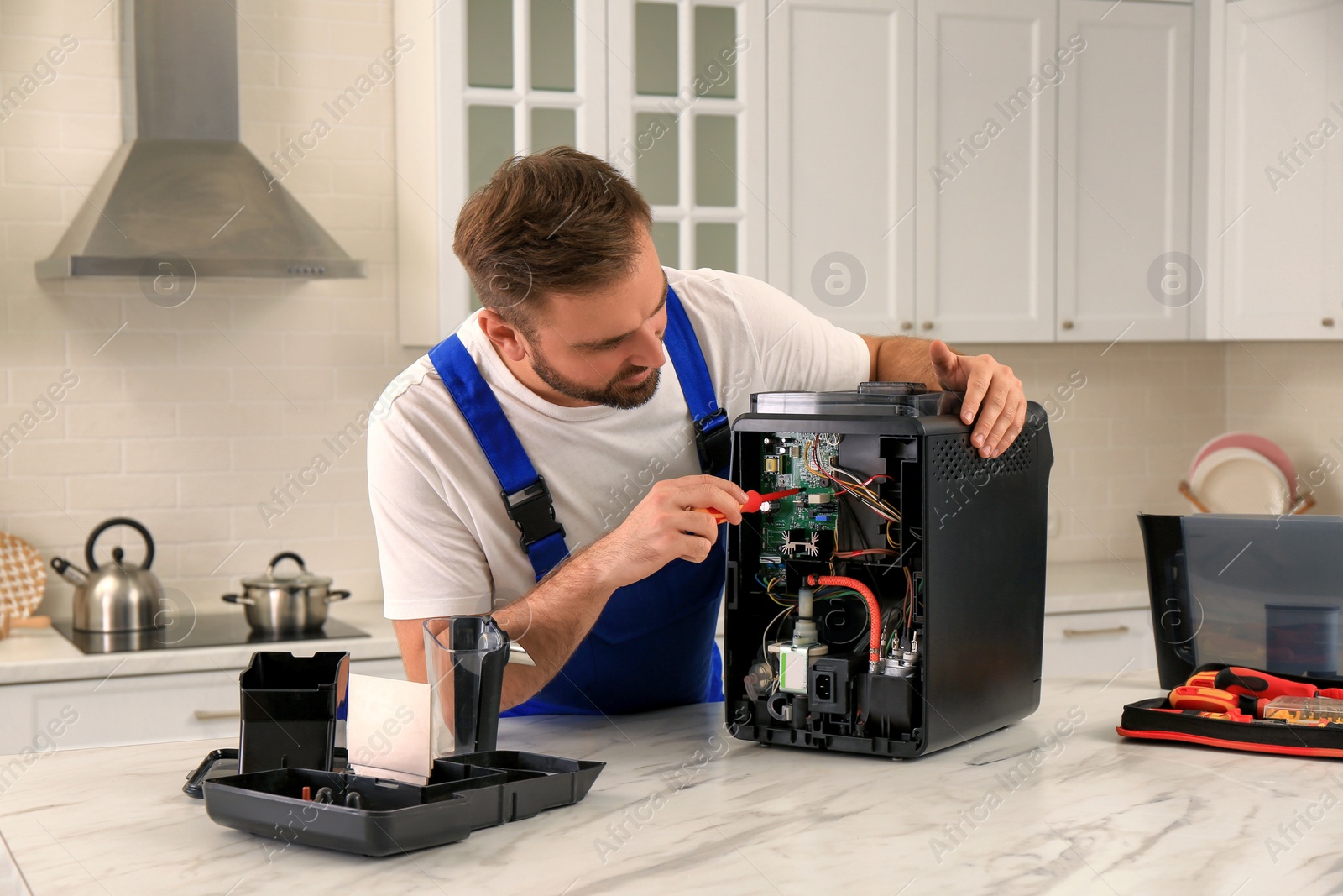 Photo of Repairman with screwdriver fixing coffee machine at table in kitchen