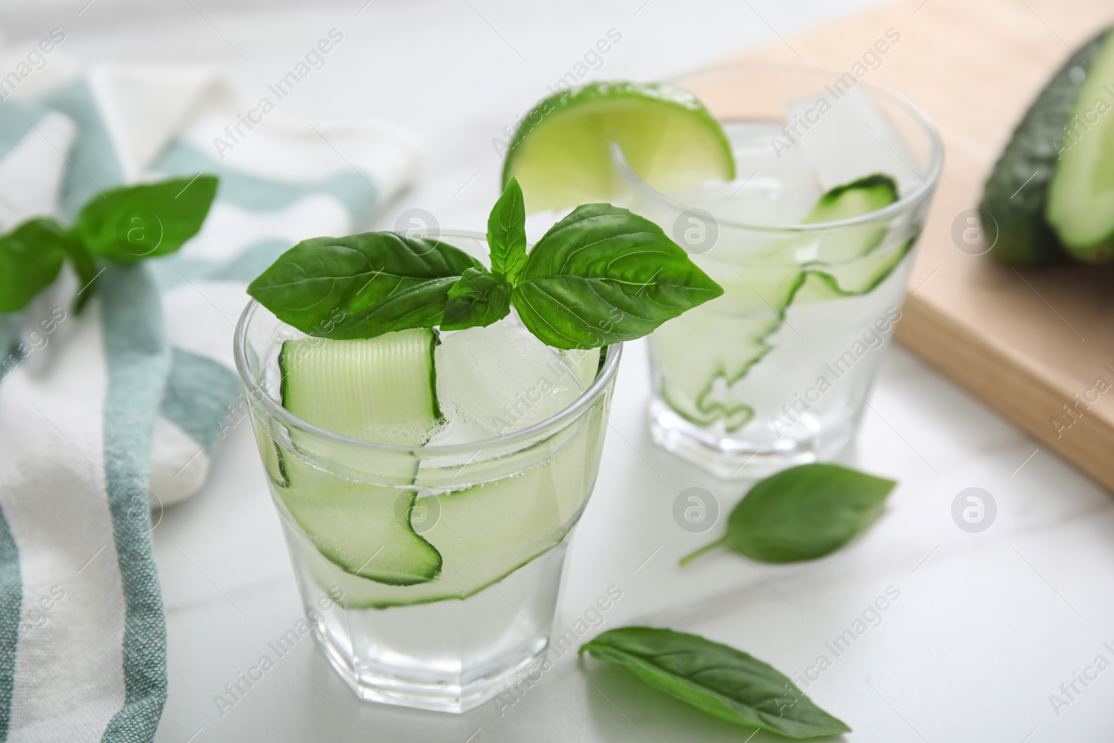 Photo of Tasty fresh cucumber water with sliced lime and basil on white marble table