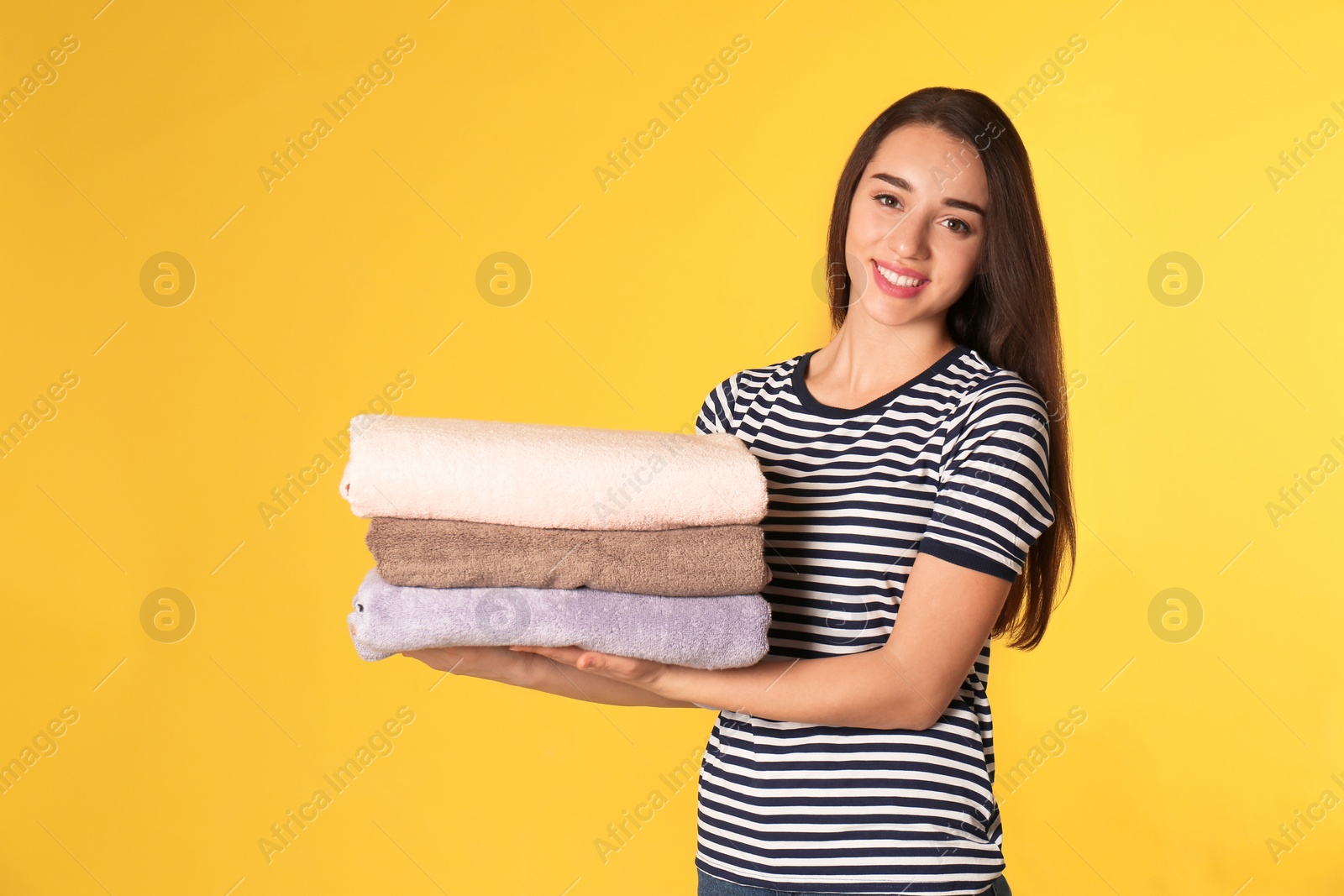 Photo of Happy young woman holding clean laundry on color background