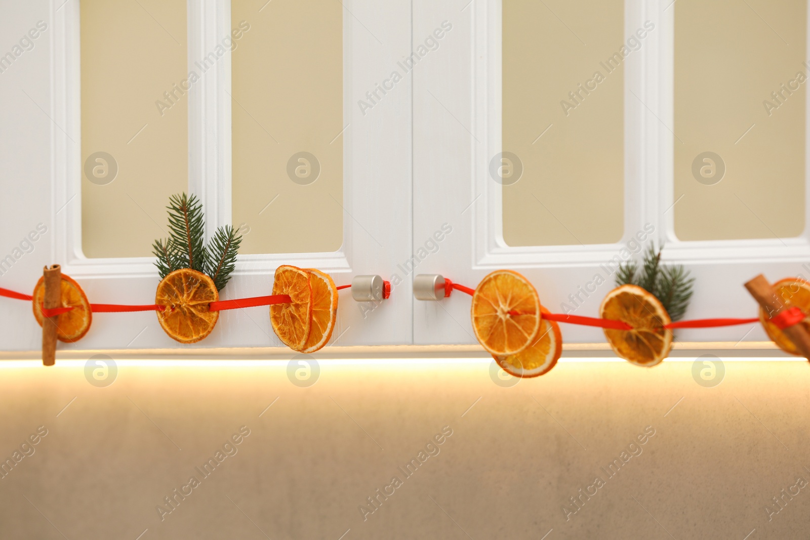 Photo of Handmade garland from dry orange slices and fir branches hanging on kitchen cabinets