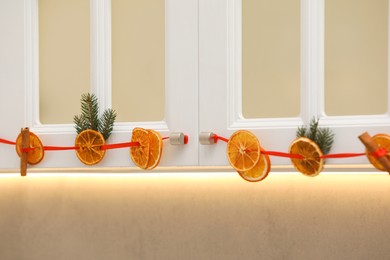 Handmade garland from dry orange slices and fir branches hanging on kitchen cabinets