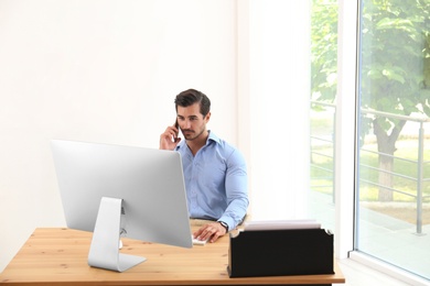 Photo of Handsome young man working with smartphone and computer at table in office