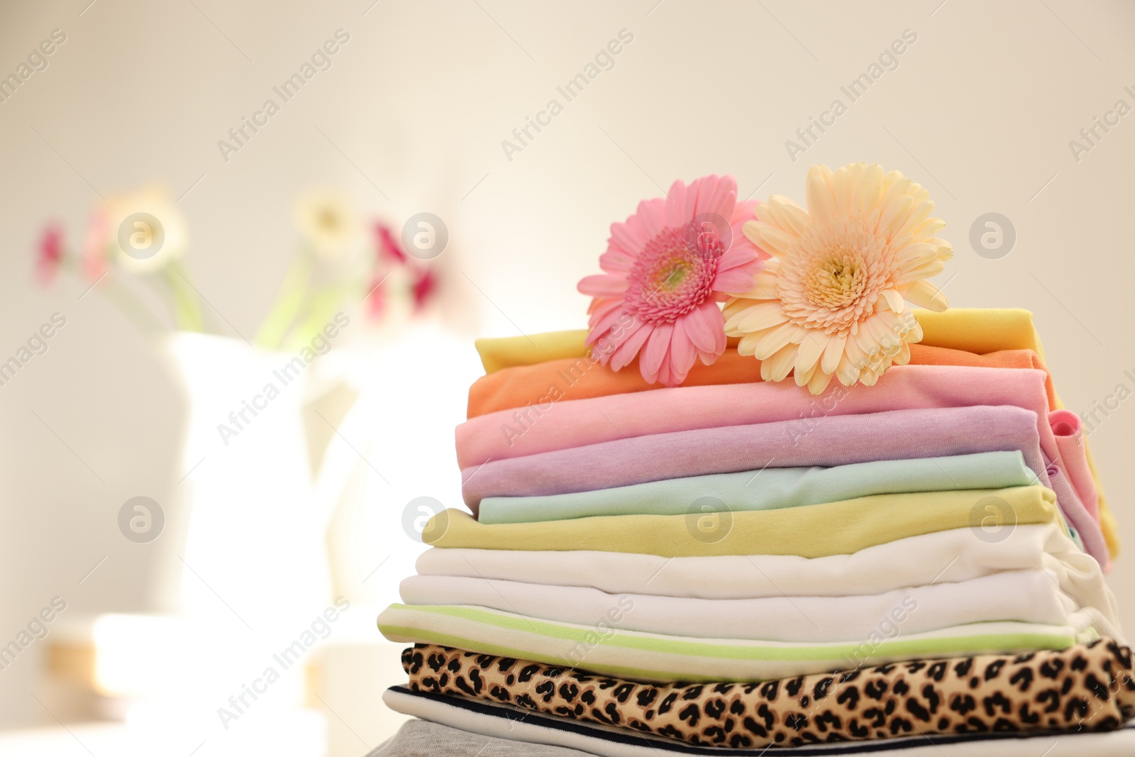 Photo of Stack of clean clothes and flowers on blurred background. Space for text