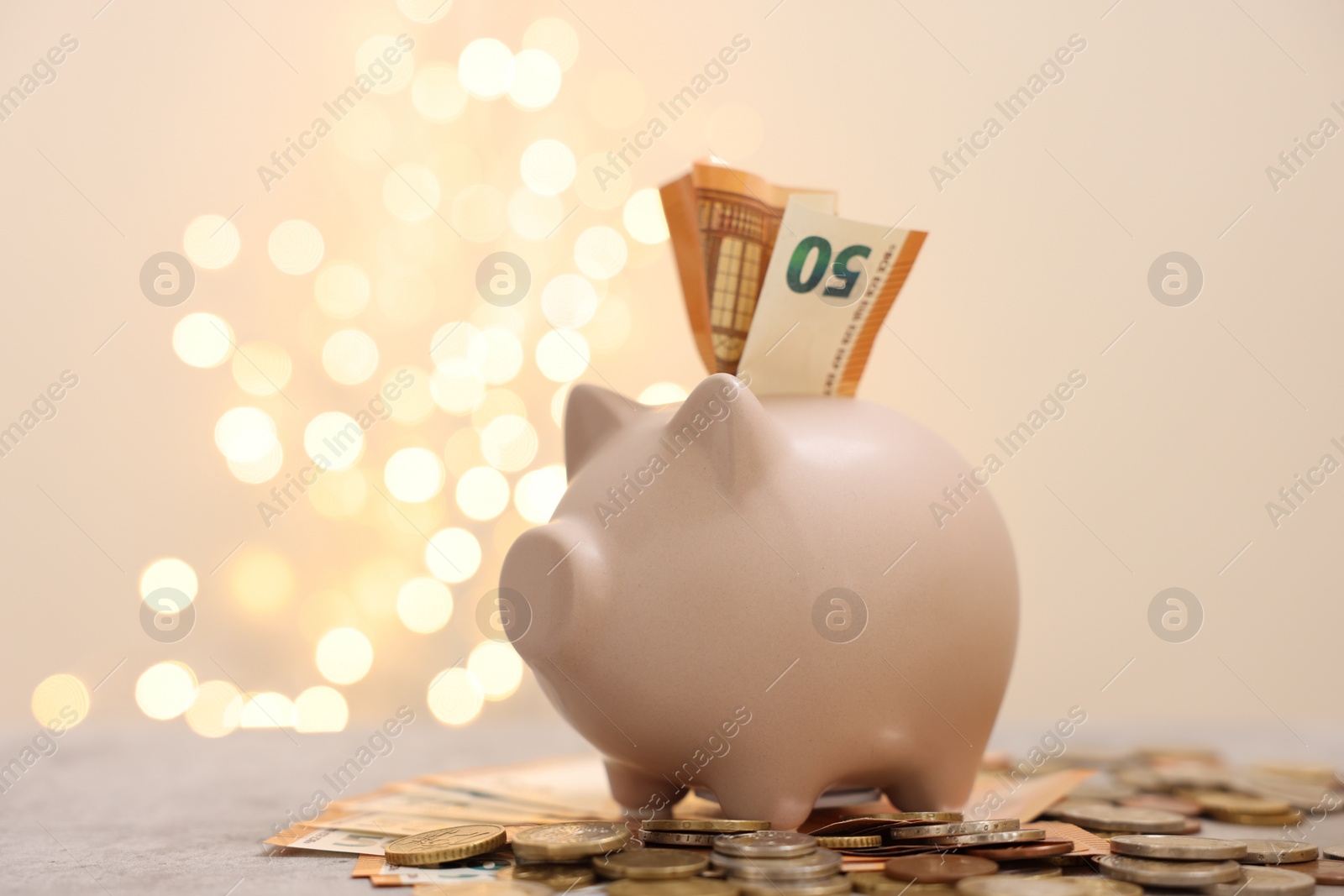 Photo of Piggy bank with euro banknote and coins on grey table against blurred lights