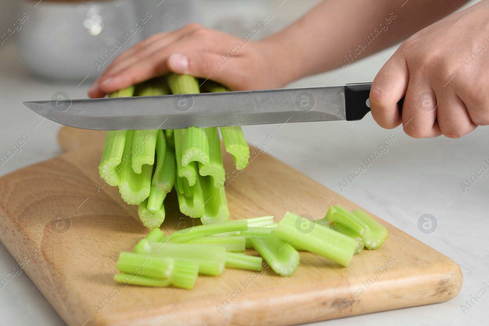 Photo of Woman cutting fresh green celery at white table, closeup