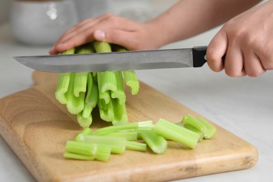 Woman cutting fresh green celery at white table, closeup