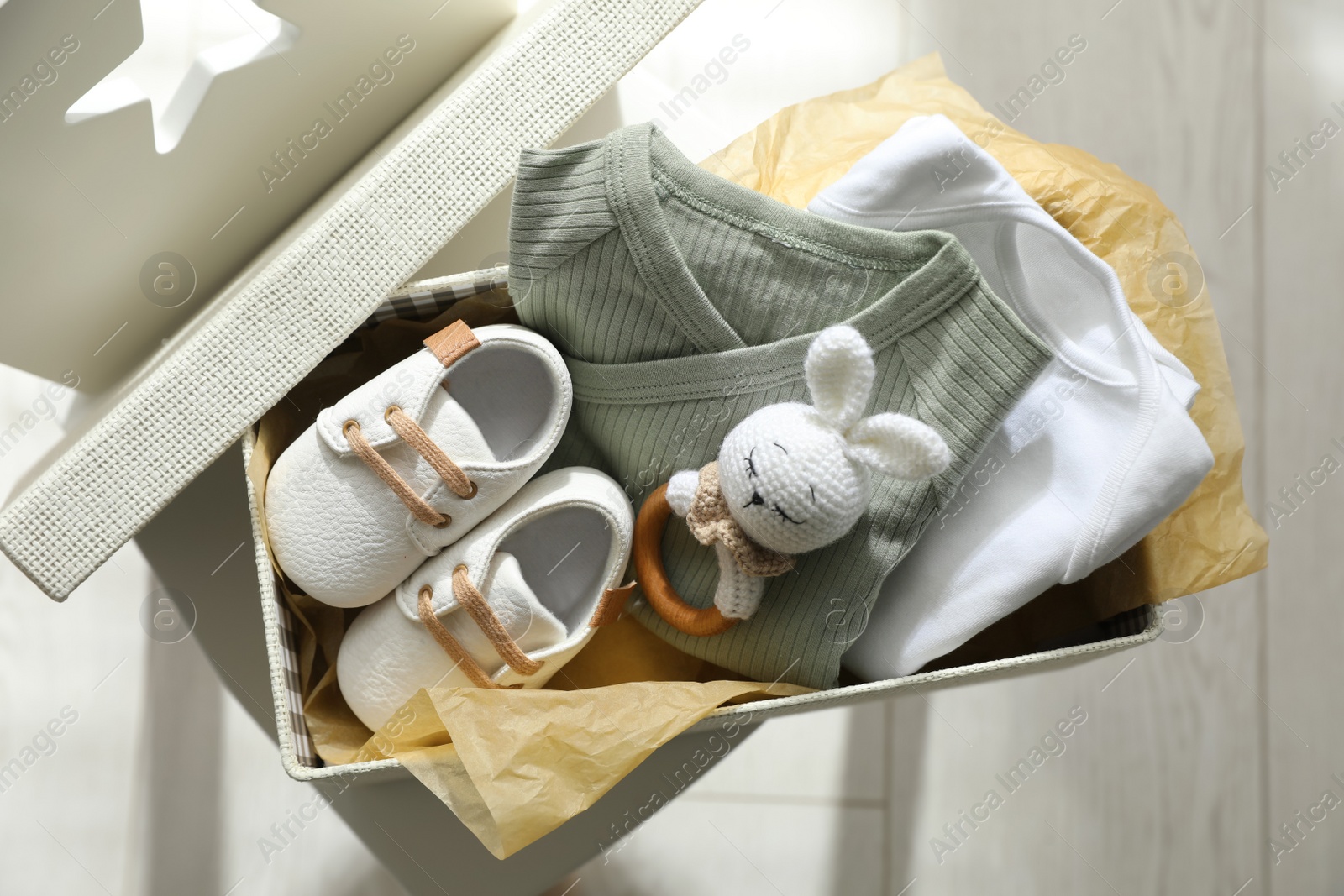 Photo of Box with baby clothes, shoes and toy on chair indoors, top view