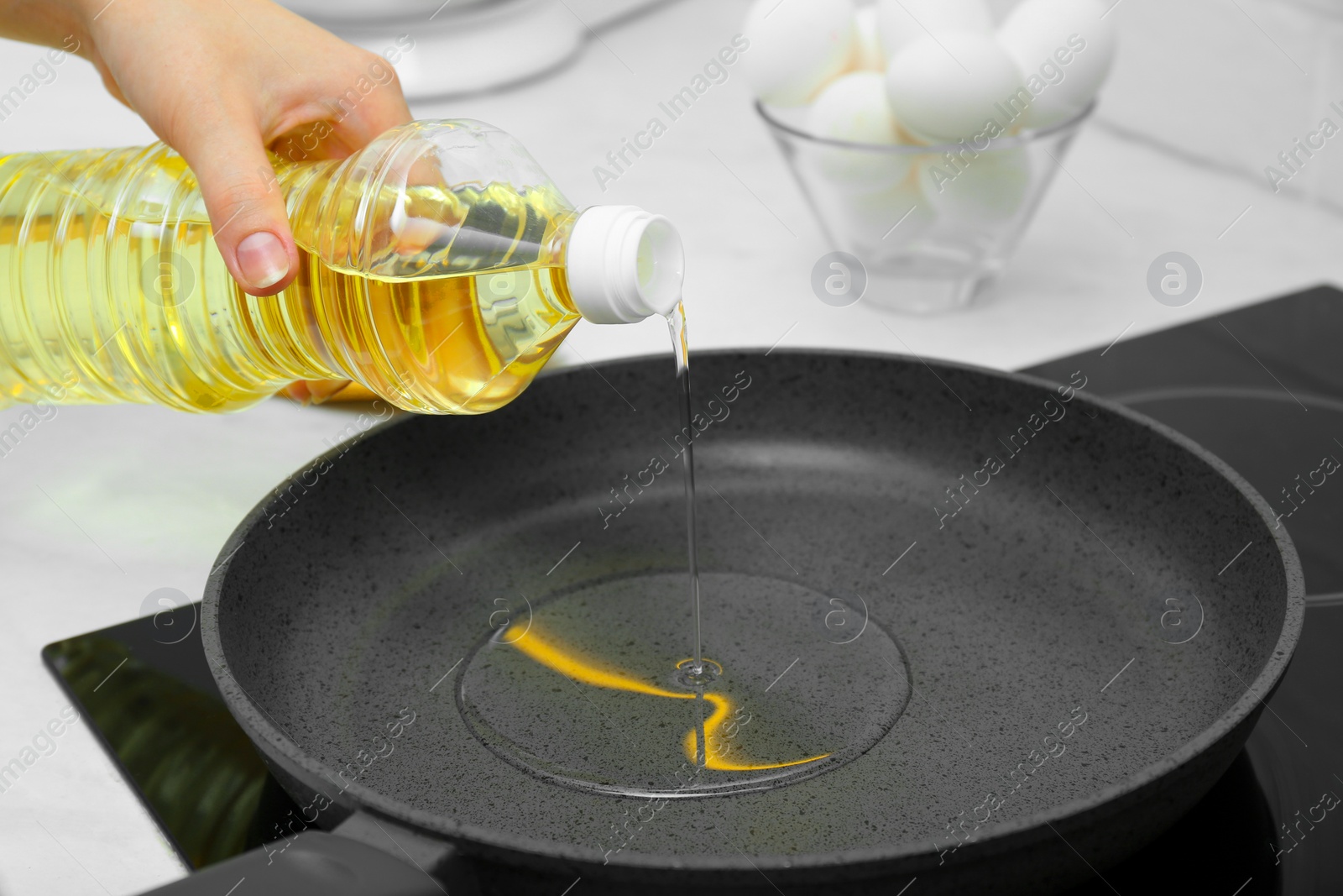 Photo of Woman pouring cooking oil from bottle into frying pan in kitchen, closeup