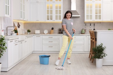 Photo of Enjoying cleaning. Happy woman in headphones listening music and mopping in kitchen