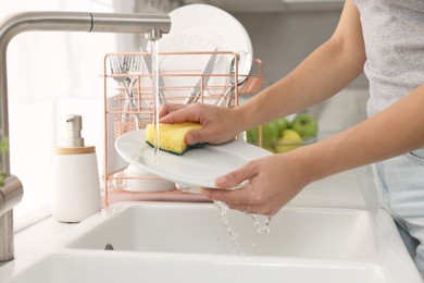 Woman washing plate at sink in kitchen, closeup