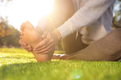 Photo of Young woman sitting barefoot on fresh green grass outdoors, closeup