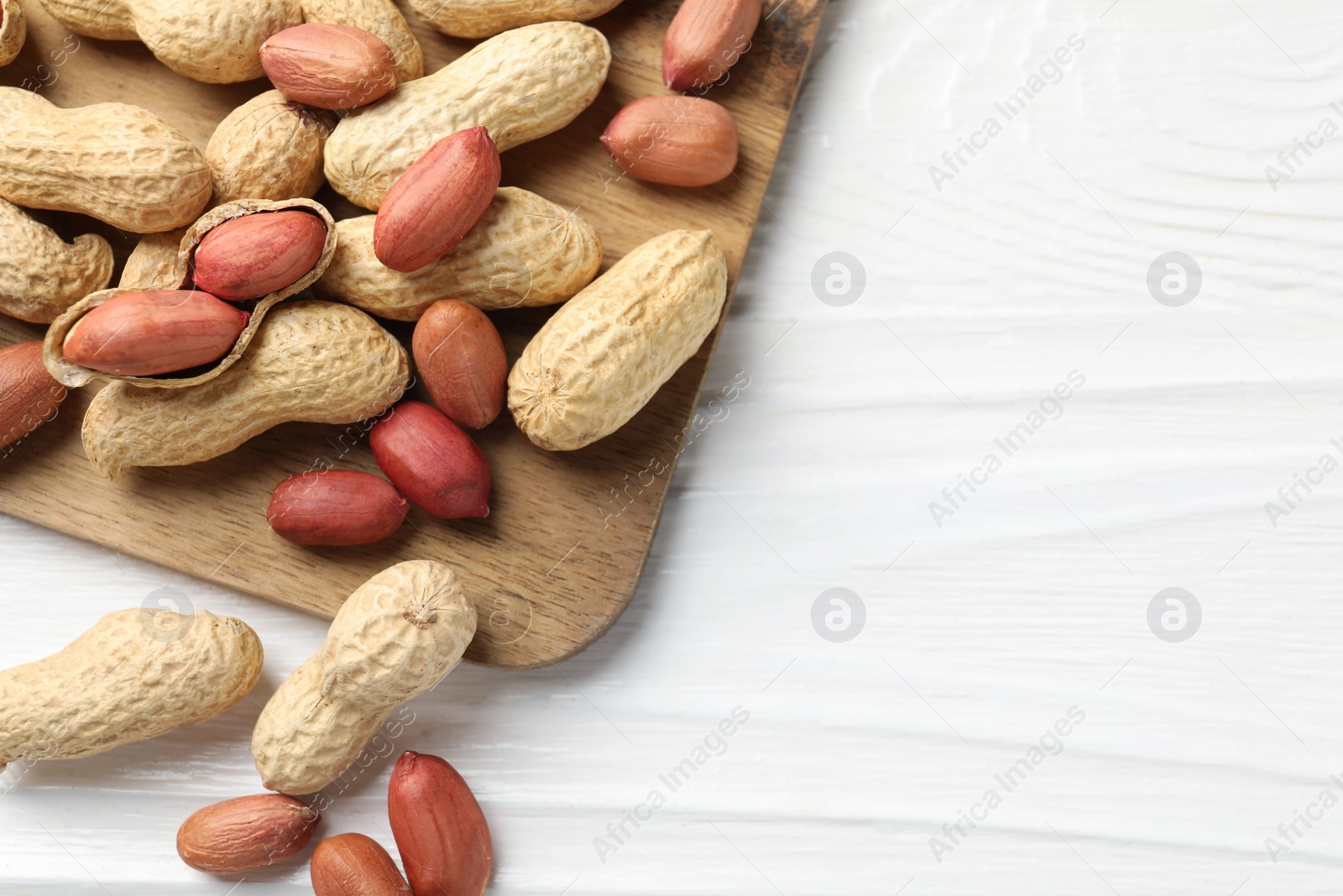 Photo of Fresh unpeeled peanuts on white wooden table, top view. Space for text